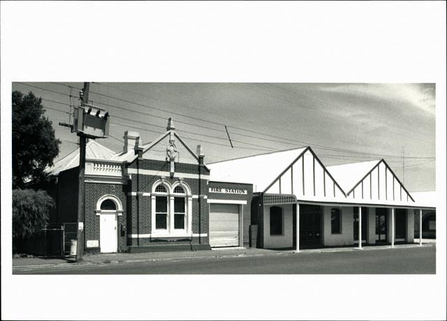 Angled front elevation of building with adjoining shops visible